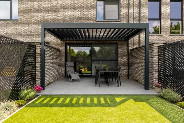 Anthrazitfarbenes Lamellendach B160 XL über einer Terrasse mit Esstisch zwischen Sichtschutzwänden