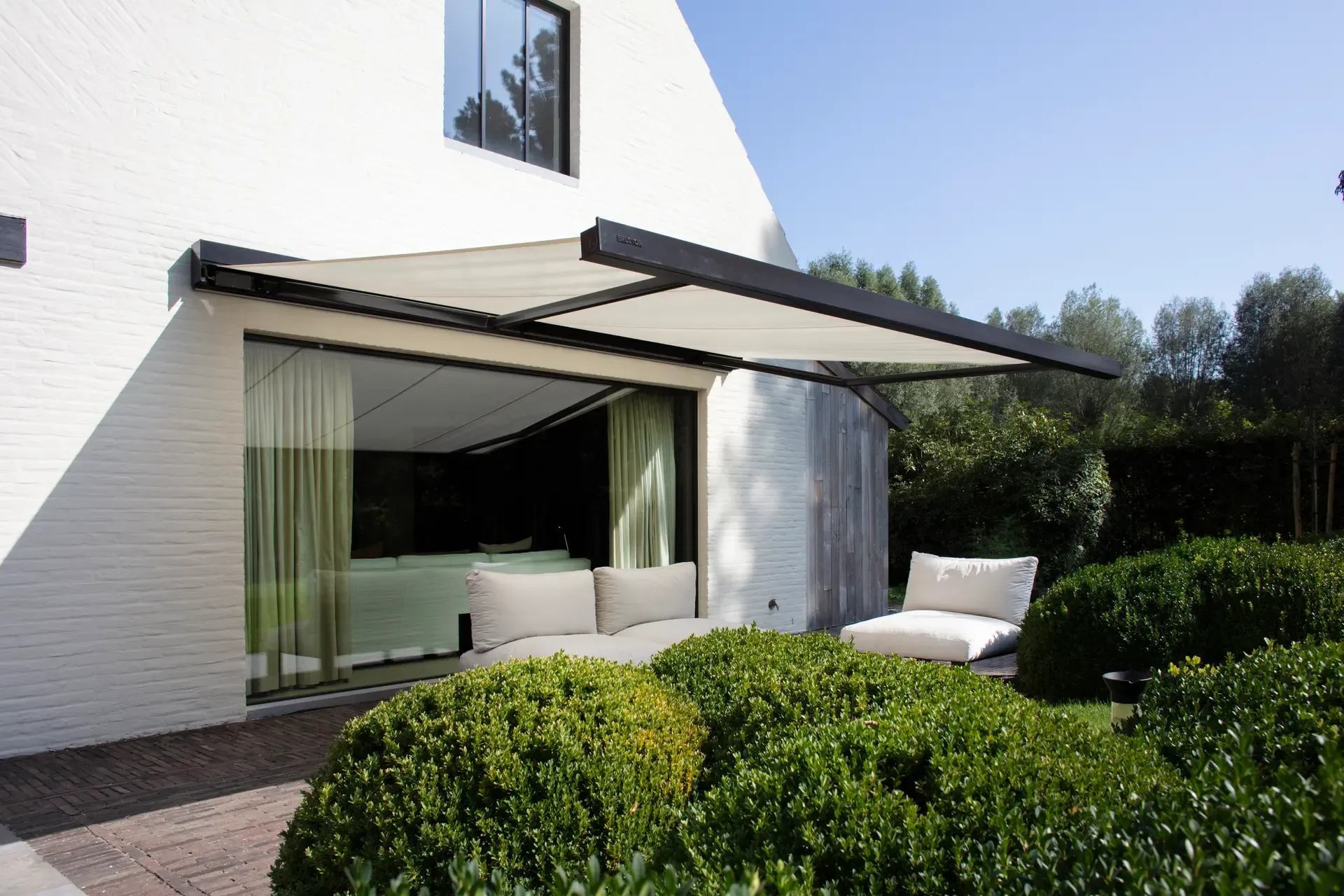 Markise B20 mit anthrazitfarbenem Gestell, ausgefahren über einer Terrasse mit Lounge an einem weissen Haus