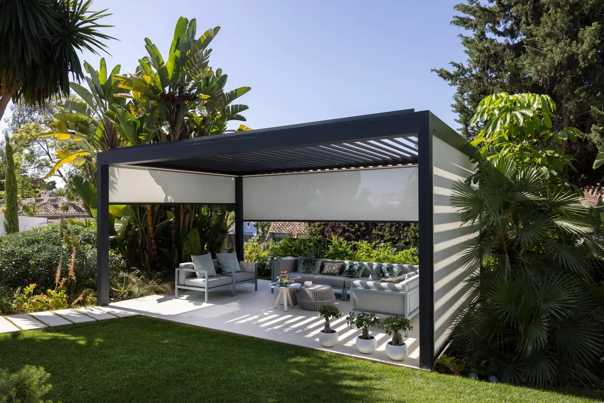 Freistehendes Lamellendach B200 XL in einem mediterranen Garten mit Palmen und Loungebereich