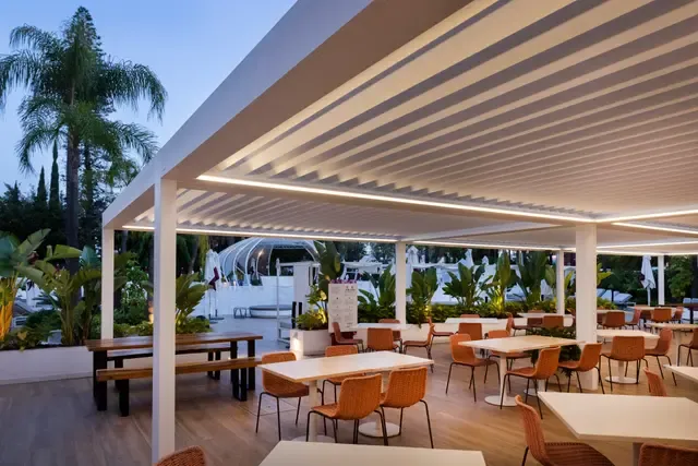 Lamellendach B200 XL mit integrierter Beleuchtung über einer Restaurantterrasse in der Dämmerung