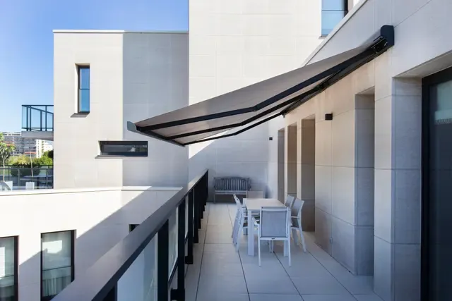 Markise B25 ausgefahren über einer Dachterrasse mit Esstisch an einem steinverkleideten Gebäude