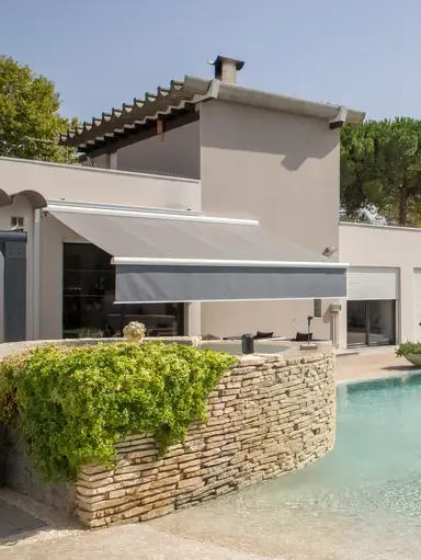 Markise B25 mit heruntergelassenem Volant über einer Poolterrasse an einem hellen Haus
