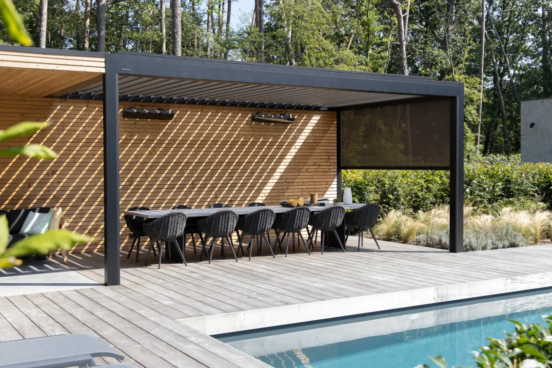 Lamellendach B250 XL über einer langen Tafel an einem Pool, dahinter Wald