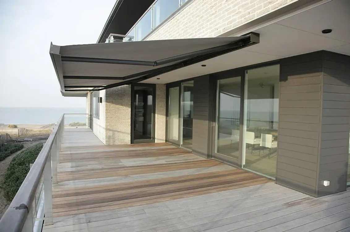 Markise B27 mit anthrazitfarbenem Gestell und Tuch, ausgefahren über einer Holzterrasse an einem modernen Haus mit Meerblick
