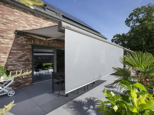 Markise B38 mit heruntergelassenem Senkrechtscreen entlang einer Terrasse an einem Backsteinhaus mit Solardach