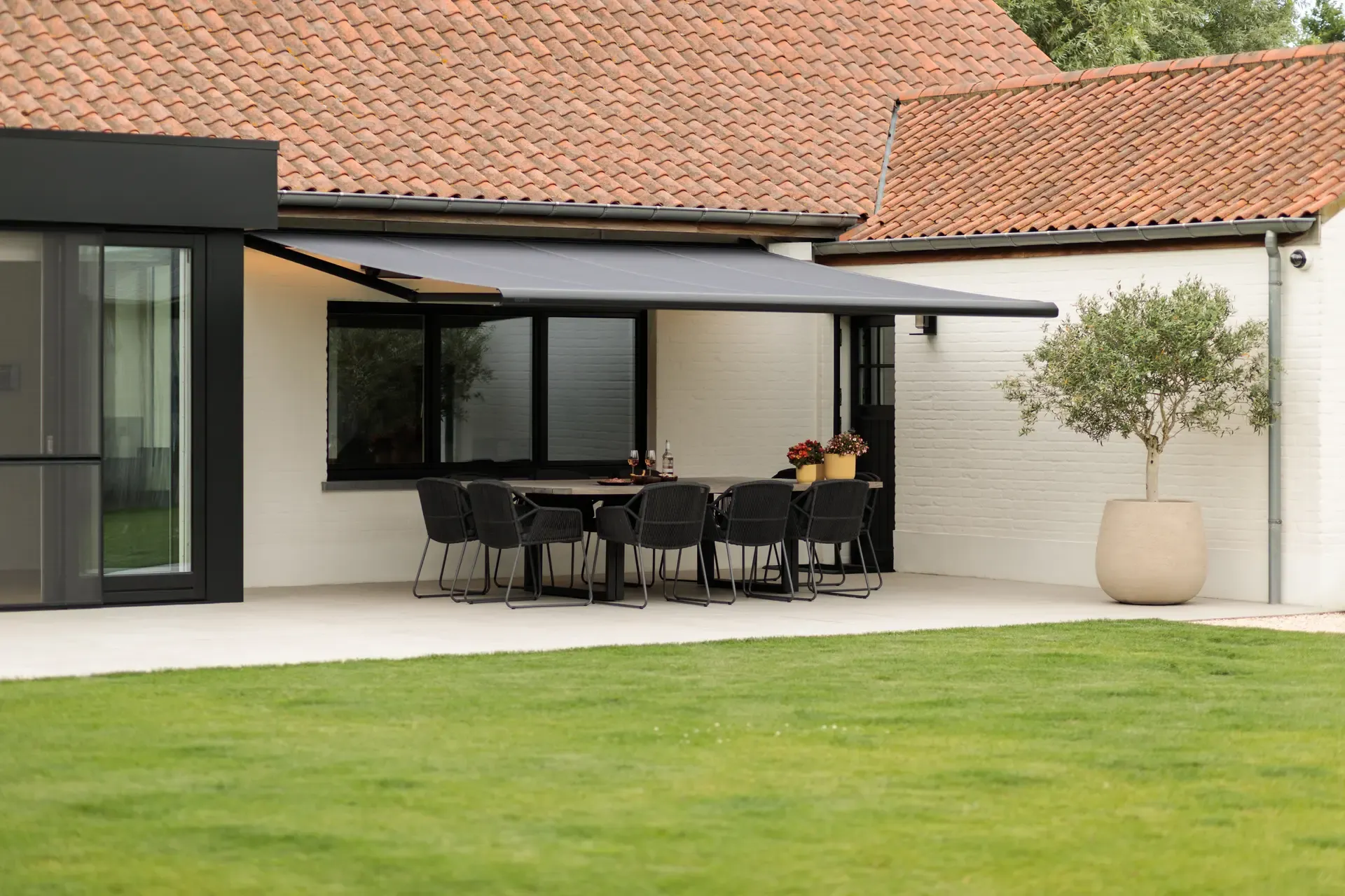 Markise B50 mit anthrazitfarbenem Gestell über einer Terrasse mit langem Esstisch an einem Landhaus