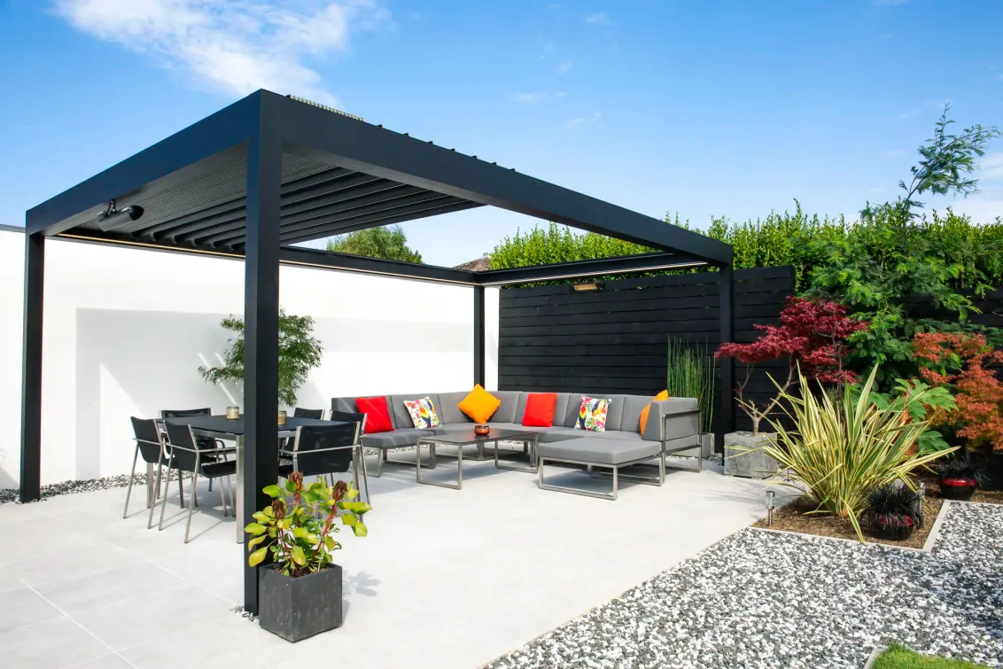 Anthrazitfarbenes Lamellendach B600 S über einer Terrasse mit Lounge und Essbereich im Garten