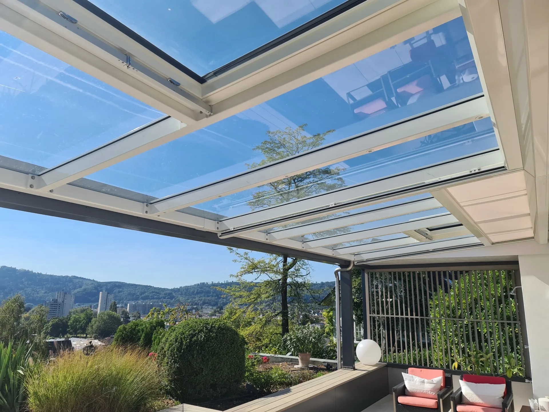 Verglastes Schiebedach über einer Terrasse mit Blick über Stadt und Hügel