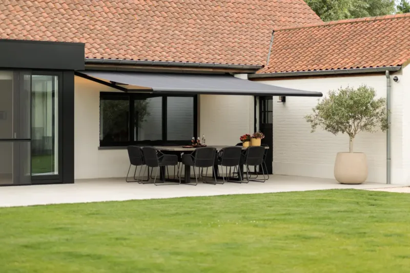 Anthrazitfarbene offene Markise ausgefahren über einer Terrasse mit Esstisch an einem Landhaus