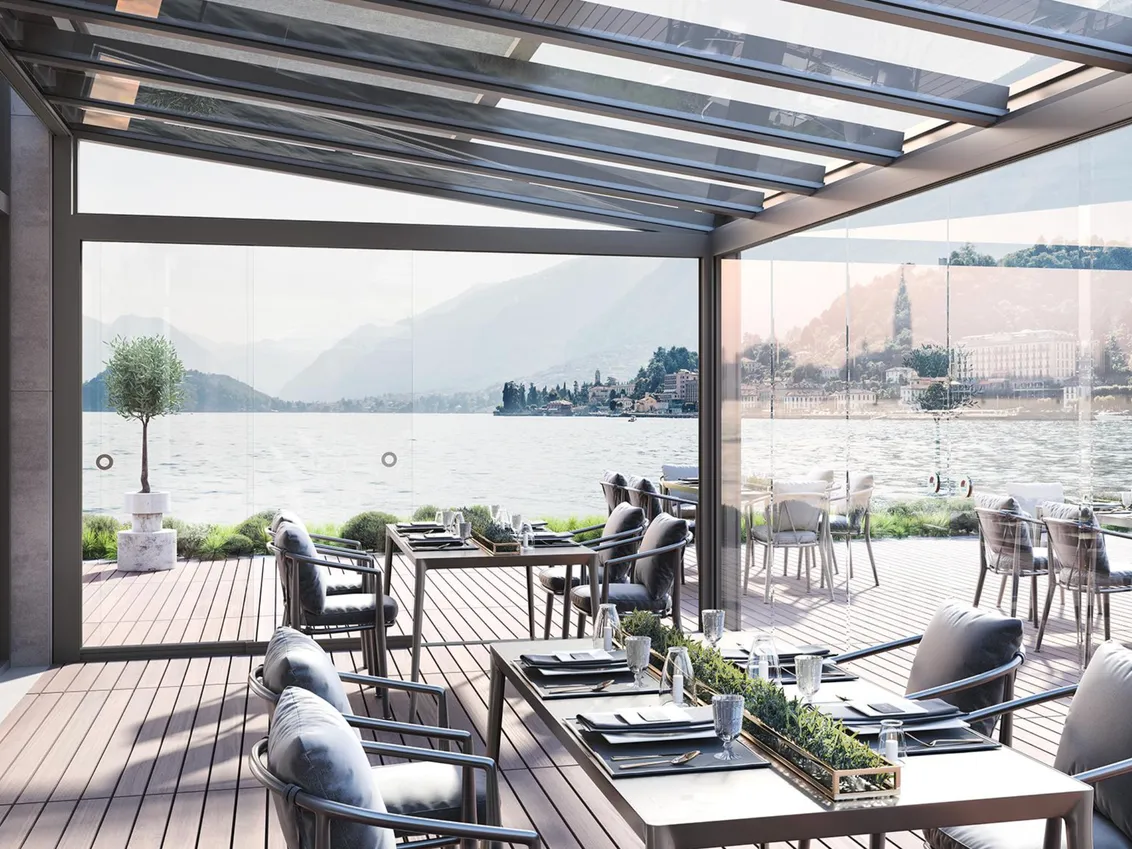 Restaurantterrasse unter einer Pergola mit Glasdach, Blick über einen See auf Berge