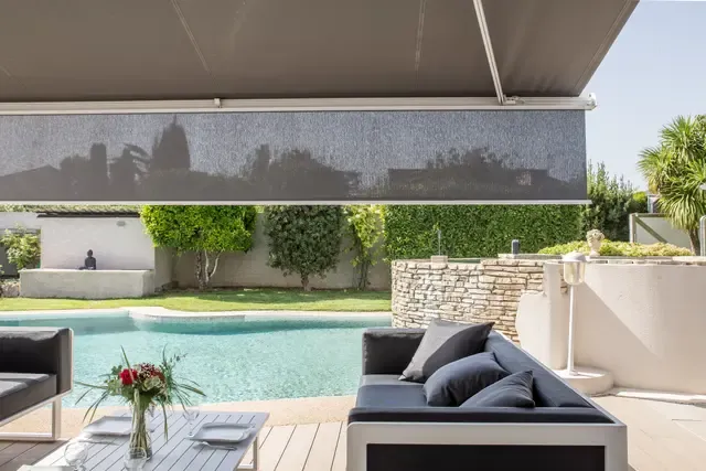 Ausgefahrene Markise mit Volant am vorderen Tuchrand über einem Loungebereich am Pool